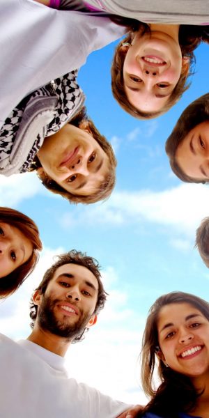 group of happy friends smiling with heads together outdoors with a blue sky in the background
